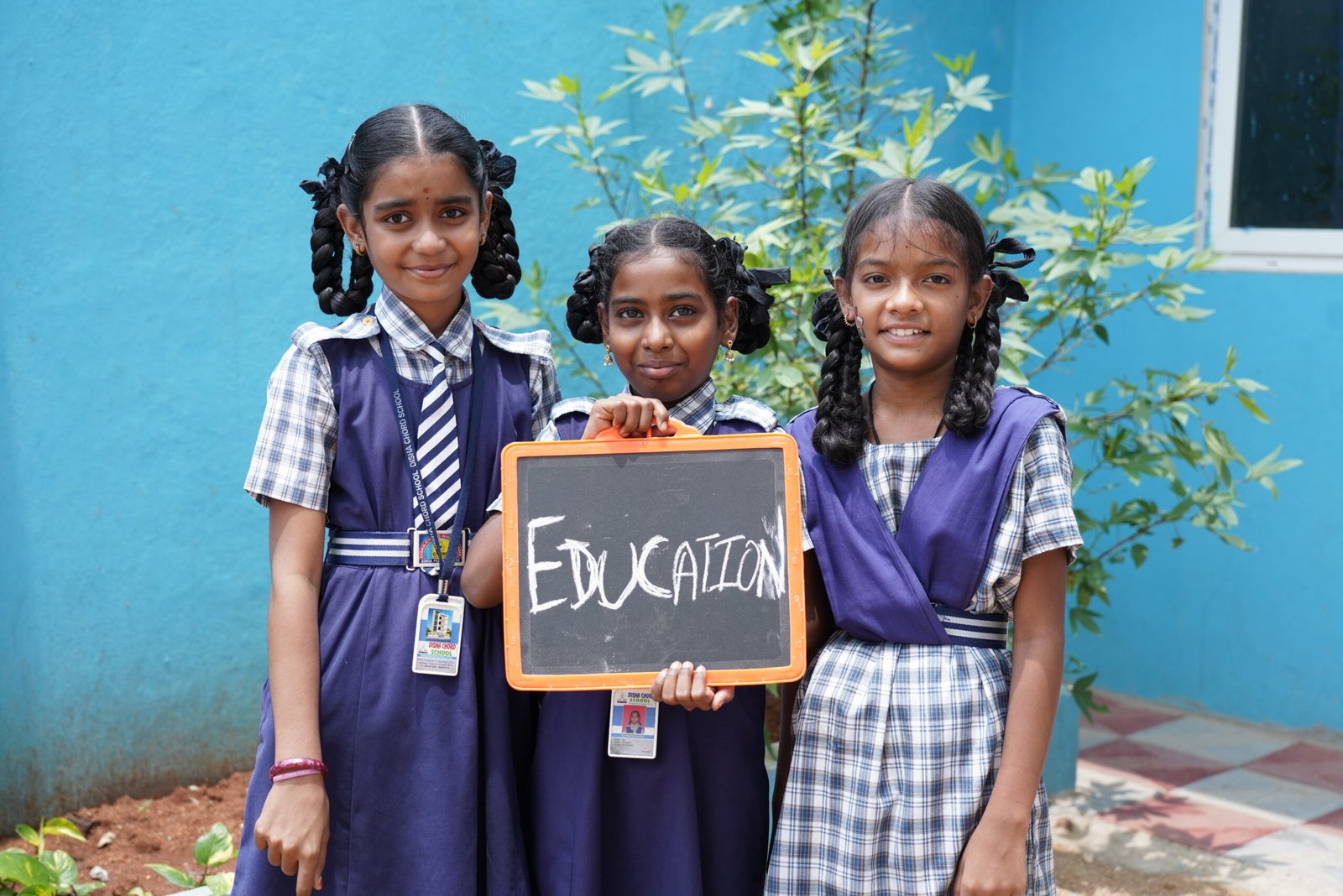 Smiling schoolgirls holding an education board, supported by an NGO in Hyderabad working towards education for childrens, skill development, and learning programs run by an education for NGO initiative.